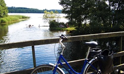 Ein Fahrrad lehnt an einem Brückengeländer, im Hintergrund macht die zugehörige Reisegruppe ihr Mittagspicknick.