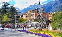 Blumenschmuck und Kunst in der von majestätischen Bergen überragten Fußgängerzone von Meran.