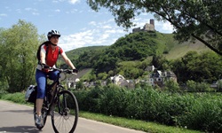 Eine Radlerin auf dem Mosel-Radweg, im Hintergrund eine der vielen Burgen entlang der Mosel.