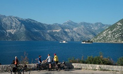 Radfahrer stehen an einer Mauer und blicken auf die Bucht von Kotor