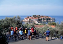 Eine Radlergruppe macht Pause am Straßenrand und blickt zur Hotelinsel Sveti Stefan in Montenegro hinab