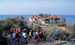 Eine Radlergruppe macht Pause am Straßenrand und blickt zur Hotelinsel Sveti Stefan in Montenegro hinab