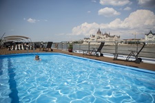 Ein Reiseteilnehmer schwimmt vor der Kulisse des Budapester Parlamentsgebäudes im Außenpool der MS Carissima.