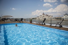 Ein Reiseteilnehmer schwimmt vor der Kulisse des Budapester Parlamentsgebäudes im Außenpool der MS Carissima.