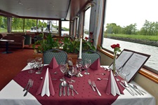 Der festlich weinrot-weiß gedeckte Tisch mit Blumen und Speisekarte im Restaurant der MS Fluvius