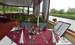 Der festlich weinrot-weiß gedeckte Tisch mit Blumen und Speisekarte im Restaurant der MS Fluvius