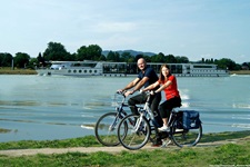 Ein Radlerpärchen auf dem Donauradweg wird von der MS Primadonna begleitet.