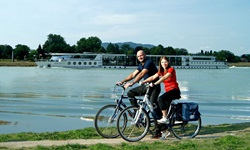 Ein Radlerpärchen auf dem Donauradweg wird von der MS Primadonna begleitet.