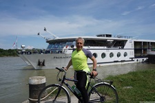 Ein Radfahrer wartet an einem Steg auf die sich nähernde MS Primadonna und posiert für ein Foto.