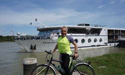 Ein Radfahrer wartet an einem Steg auf die sich nähernde MS Primadonna und posiert für ein Foto.