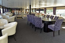 Der gemütliche Salon mit beigen Clubsesseln und einem Tisch mit weiß-blauen Sesseln mit Blick zur Tanzfläche und der Bar auf der MS Serena