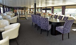 Der gemütliche Salon mit beigen Clubsesseln und einem Tisch mit weiß-blauen Sesseln mit Blick zur Tanzfläche und der Bar auf der MS Serena