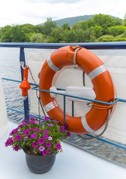 Rettungsring in orange-weiß an der Reling der MS Allure. Im Vordergrund ein Blumentopf mit lila Blumen