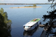 Blick über einen See mit einer kleinen Insel der Masurischen Seenplatte und die an einem Holzsteg angelegte MS Classic Lady