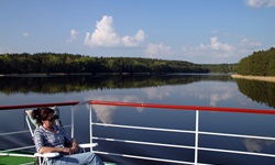 Eine Frau auf dem Sonnendeck der MS Classic Lady genießt die umwerfende Landschaft in Masuren