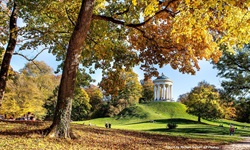 Blick auf den von herbstlich gefärbten Bäumen umrahmten Monopteros im Englischen Garten von München.