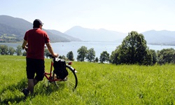 Ein Radfahrer steht mit seinem Rad auf einer saftig grünen Wiese und blickt zum Chiemsee und den dahinterliegenden Alpen