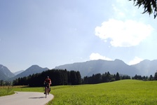 Ein Radler fährt an Wiesen und Wälder vorbei, währen im Hintergrund die Alpen zu erkennen sind