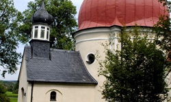 Eine große Kapelle mit einem runden Dach - davor sind am Holzgeländer zwei Räder abgestellt