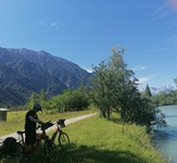 Radfahrer am Ufer eines Flusses mit den Alpen im Hintergrund bei der Münchner Seenrunde
