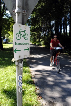 Ein Verkehrsschild mit Beschilderung des Isarradwegs, auf dem ein Radfahrer entlang fährt