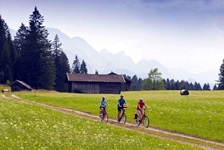 Drei Radler fahren auf den typischen Feldwegen in Bayern und mit gigantischer Bergkulisse auf der Strecke der bayerischen Seenrunde bzw. der Münchner Seen entlang