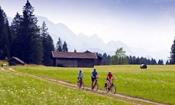Drei Radler fahren auf den typischen Feldwegen in Bayern und mit gigantischer Bergkulisse auf der Strecke der bayerischen Seenrunde bzw. der Münchner Seen entlang