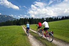 Drei Fahrradfahrer radeln auf einem Feldweg in Richtung Wald auf der Strecke der bayerischen Seenrunde bzw. der Münchner Seen