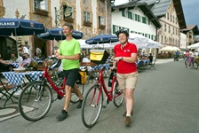 Zwei Radfahrer schieben ihre Räder durch eine Fußgängerzone auf der Strecke der Münchner Seen, in der es viele Cafés und Restaurants gibt.