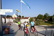 Drei Radfahrer radeln auf einer Brücke über die Isar