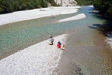 Zwei Fahrradfahrer sitzen im Flussbett der Isar und kühlen ihre Füße ab