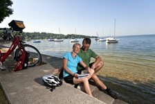 Zwei Radfahrer sitzen an einer Promenade - die Räder hinter sich abgestellt - an der Radstrecke der Münchner Seenrunde