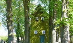 Eine Allee zu einem gelb-grünen Holzhaus