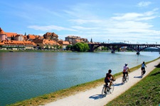 Drei Radlerinnen fahren am Flusslauf der Mur entlang auf eine Brücke zu.