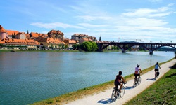 Drei Radlerinnen fahren am Flusslauf der Mur entlang auf eine Brücke zu.