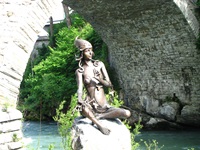 Die Statue der Flussgöttin Murna sitzt bei Murnau auf einem Stein; über ihr wölbt sich ein Brückenbogen.