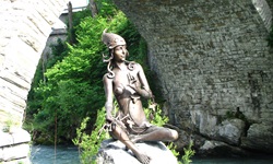 Die Statue der Flussgöttin Murna sitzt bei Murnau auf einem Stein; über ihr wölbt sich ein Brückenbogen.