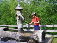 Eine Radlerin füllt an einem originell gestalteten Holzbrunnen ihre Trinkflasche auf.