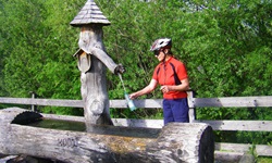 Eine Radlerin füllt an einem originell gestalteten Holzbrunnen ihre Trinkflasche auf.