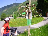 Eine Radlerin bewundert ein altes Fahrrad, das über einem Hinweisschild auf den Mur-Radweg aufgehängt ist.