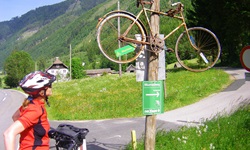 Eine Radlerin bewundert ein altes Fahrrad, das über einem Hinweisschild auf den Mur-Radweg aufgehängt ist.