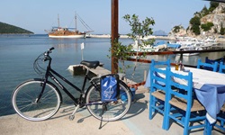 Ein Fahrrad steht an der Promenade zum Meer an einem Restaurant. Im Hintergrund ist das angelegte Schiff Panagiota zu sehen