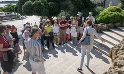 Eine Gruppe Touristen nimmt an einer Stadtbesichtung in Sibenik teil - eine Frau erklärt und zeigt auf die Mauern einer Treppe