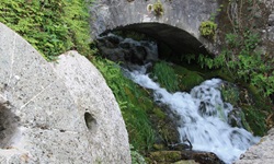 Zwei Mühlsteine liegen unterhalb einer romantischen Steinbrücke, die über einen sprudelnden Wildbach in Dalmatien hinwegführt.