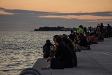 Menschen sitzen am Steg in Zadar in Kroatien und bewundern den Sonnenuntergang