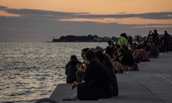 Menschen sitzen am Steg in Zadar in Kroatien und bewundern den Sonnenuntergang
