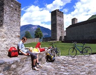 Ein Radlerpärchen hat es sich auf einer Mauer, die den Hof der Burg Castelgrande in Bellinzona begrenzt niedergelassen und macht eine wohlverdiente Pause.