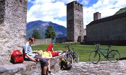 Ein Radlerpärchen hat es sich auf einer Mauer, die den Hof der Burg Castelgrande in Bellinzona begrenzt niedergelassen und macht eine wohlverdiente Pause.