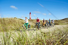 Eine Radlergruppe fährt an einem von Dünen umrahmten nordfriesischen Leuchtturm vorbei.