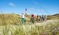 Eine Radlergruppe fährt an einem von Dünen umrahmten nordfriesischen Leuchtturm vorbei.